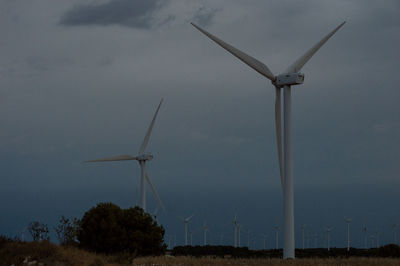 Low angle view of wind turbines on field against sky