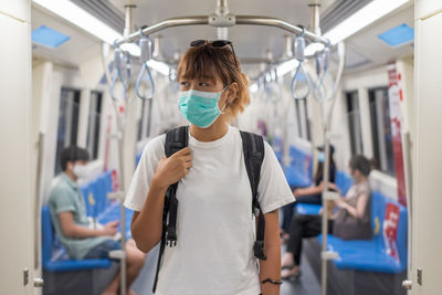 Young asian backpacker woman wear face mask travel to the city by subway or skytrain, covid-19