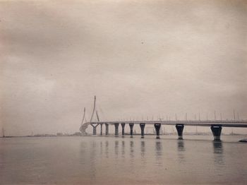 Silhouette cranes by sea against sky