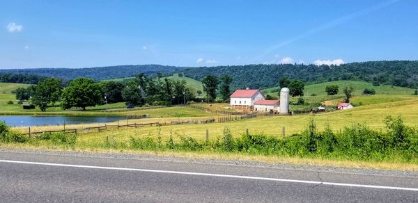 Scenic view of field by houses and trees against sky