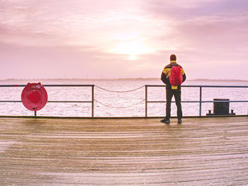 Rear view of man standing by sea against sky during sunset