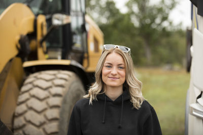 Portrait of smiling young woman standing next to excavator