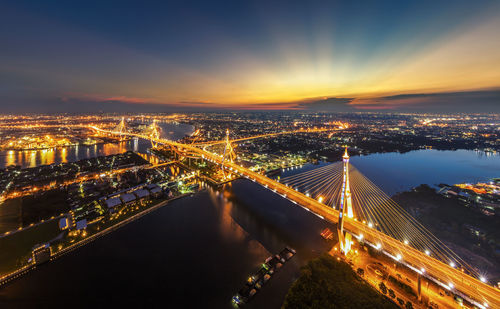 Illuminated bhumibol bridge over chao phraya river against sky during dusk