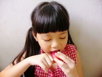 Close-up of girl eating fruit while sitting against wall 