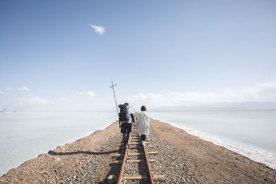 Rear view of couple walking on railroad track against sky