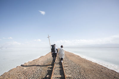 Rear view of men standing by sea against sky