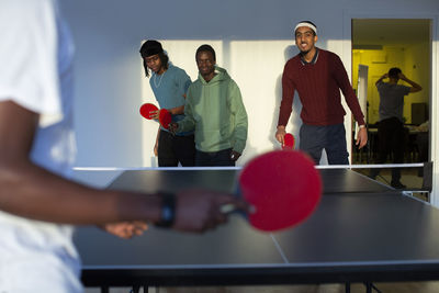 Excited friends playing table tennis in games room