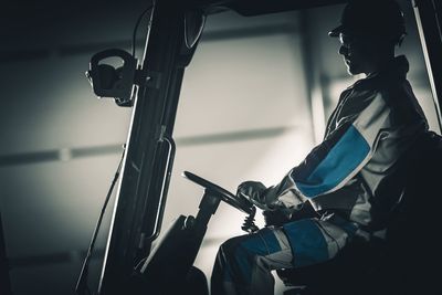 Side view of manual worker driving forklift at factory