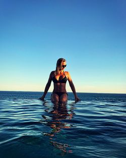 Sensuous woman in infinity pool by sea against clear blue sky