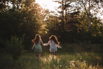 Back view of lesbian couple holding hands while running in forest