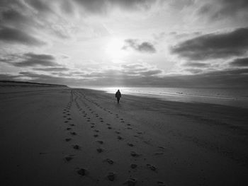 Woman walking on an empty beach at sunset with dramatic sky