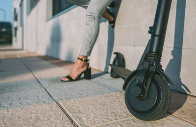 Low section of woman standing by electric scooter on footpath