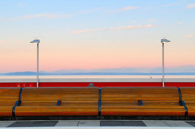 Empty benches against sky during sunset