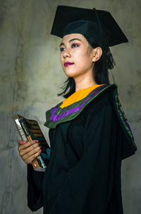 Side view of young woman using phone while standing against wall