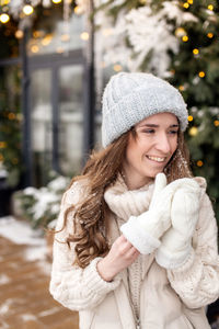 The smiling girl takes off her mittens to remove the snow from her face and hat