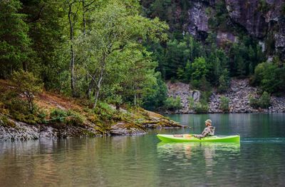 Side view of man sailing boat in lake against trees