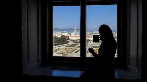 Silhouette man looking through window