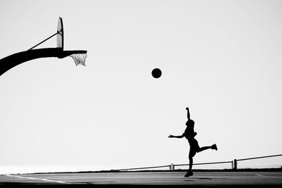 Silhouette man playing basketball on court against clear sky