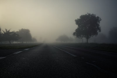 Empty road amidst trees against sky during foggy weather