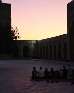 People sitting outside building against sky during sunset