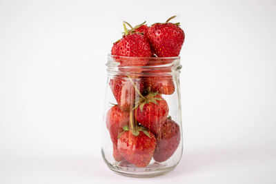 Close-up of strawberries in glass jar against white background