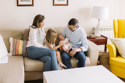 Happy family of four with the new newborn baby. older sister, dad and mum in the sofa