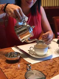 Midsection of woman pouring tea at table