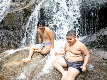 Shirtless father and son enjoying waterfall