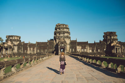 Rear view of woman walking towards historical building against blue sky