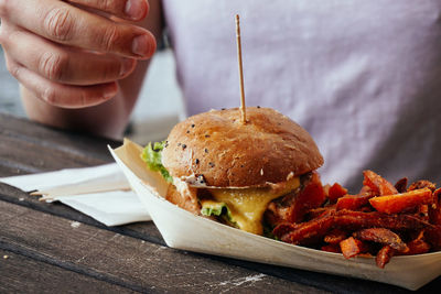 Midsection of man sitting by burger on table