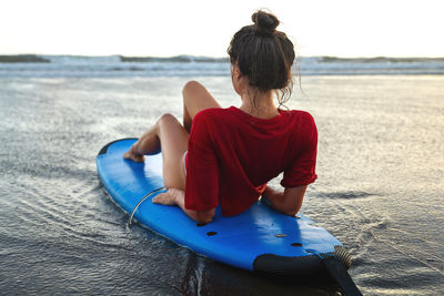 Woman sitting on surfboard on the beach after her surfing session