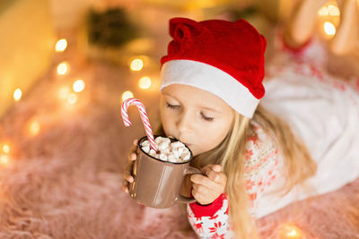 Close-up of girl drinking coffee with marshmallow with christmas lights