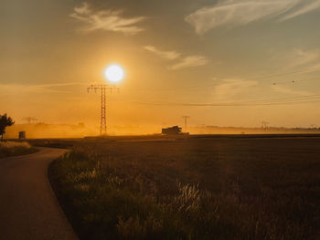 Road amidst field against sky during sunset