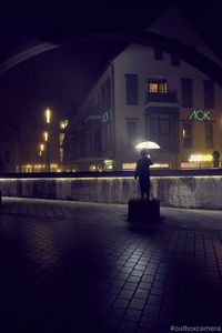 Rear view of person standing on footpath at night