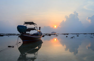 Fishing boat moored in sea against sky during sunset