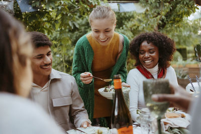 Smiling woman serving salad to male and female friends at dinner party in back yard