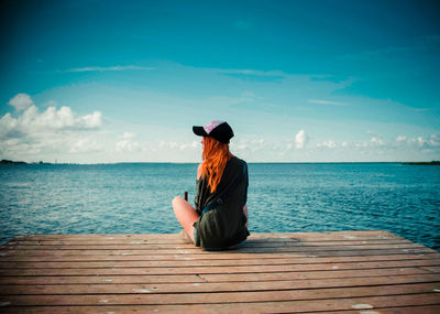 Woman sitting on rock looking at sea against sky