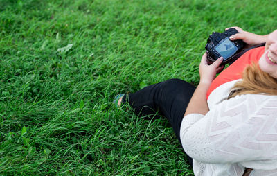 Low section of woman holding camera while sitting on grass outdoors