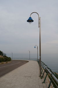 Street light on footpath by sea against sky