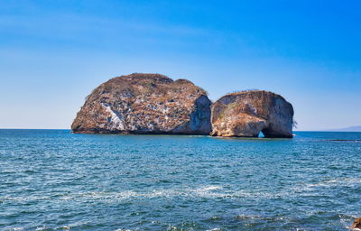 Rock formation in sea against clear blue sky