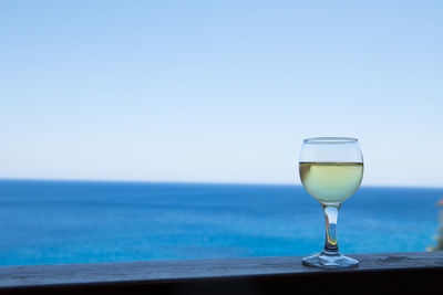 Wine glass against blue sea against clear sky