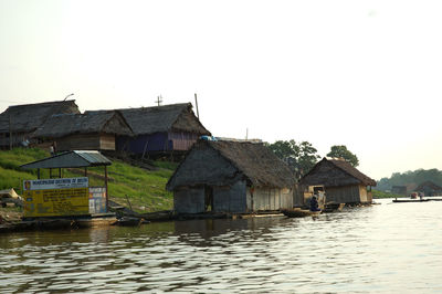 Houses by river against buildings against clear sky