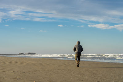 Rear view of a man walking on beach against sky
