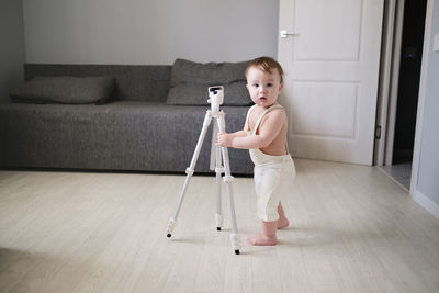 Cute toddler boy in overalls playing with tripod for photos