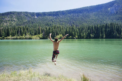 Rear view of man jumping into lake against mountain