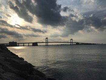Bridge over calm sea against cloudy sky
