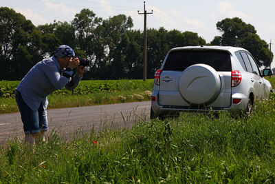 Man photographing by grassy field on road