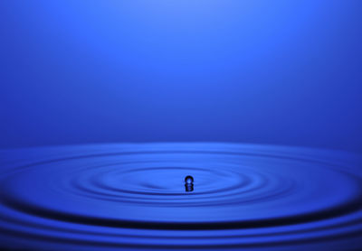 Close-up of drop falling on water against blue background