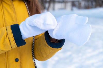 Young woman in yellow jacket putting on white mittens.