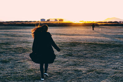 Rear view of mid adult woman walking on beach against clear sky during sunset
